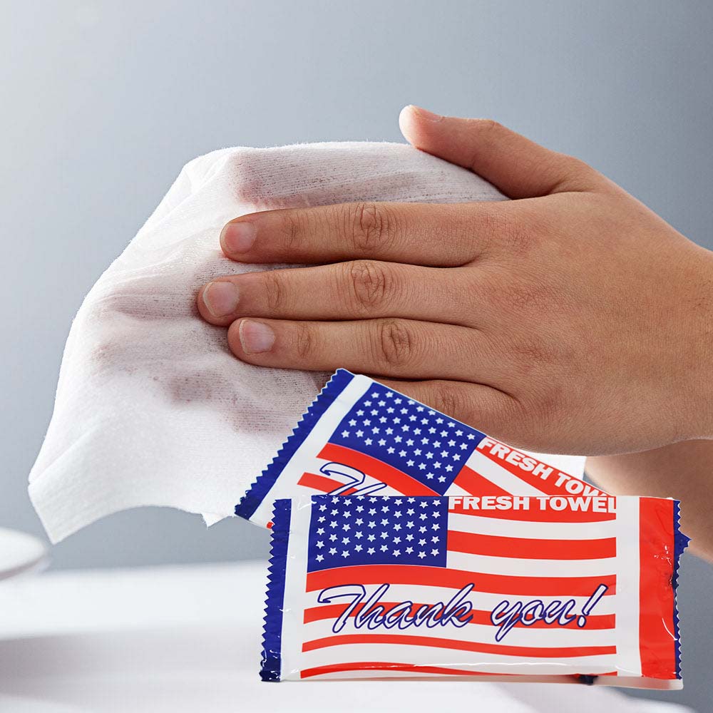 Hands shown using wet wipes with product image of wet wipes in package in front of the photo. Package shows an American flag with the text, "Thank you!" and the company name: "Fresh Towel".