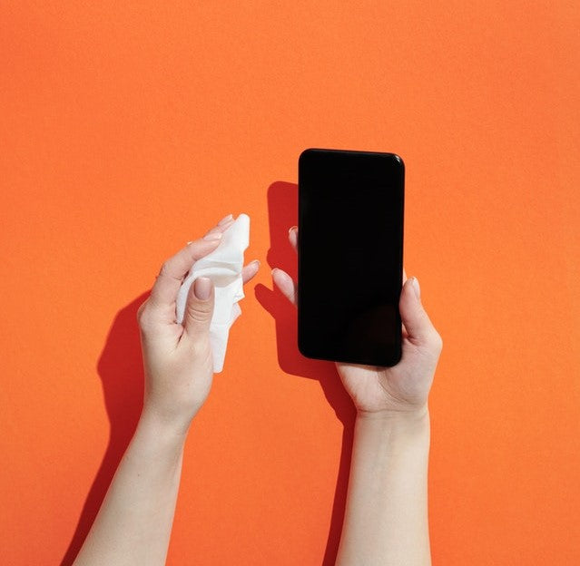 Orange background with hands wiping smartphone with a wet wipe.